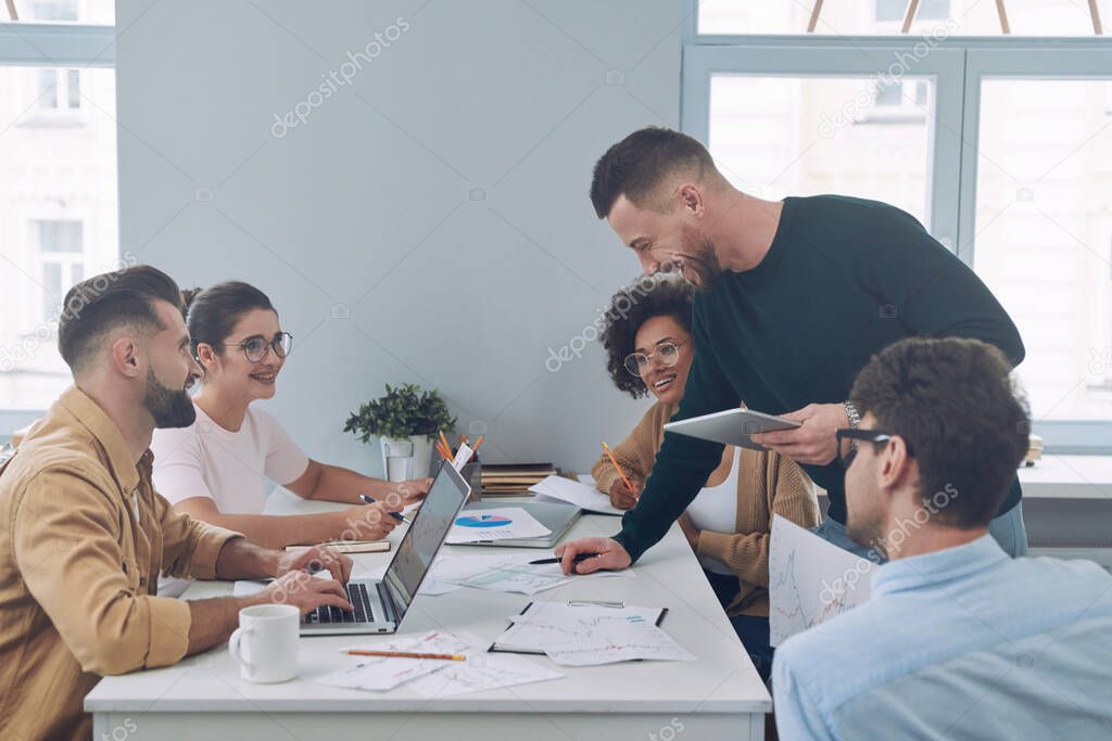 Group of confident young people in smart casual wear discussing business while having meeting in office