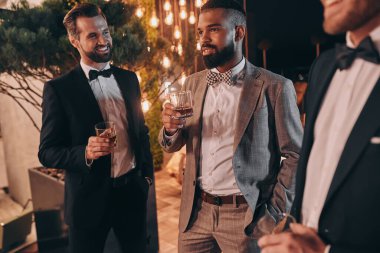Takım elbiseli, elinde viski bardaklarıyla eğlenen üç mutlu adam.