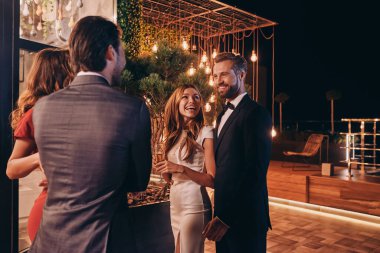 Resmi kıyafet giyen bir grup insan lüks bir partide vakit geçirirken iletişim kuruyor ve gülümsüyor.