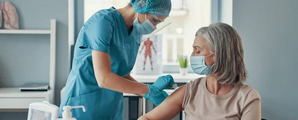 Jeune infirmière faisant la vaccination à la femme mûre tout en travaillant à l'hôpital — Photo