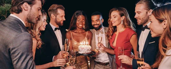 Gruppo di persone in abbigliamento formale che tengono la torta con le candele mentre festeggiano il compleanno tra amici — Foto Stock