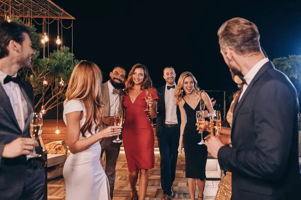 Grupo de gente hermosa en ropa formal comunicándose y sonriendo mientras pasa tiempo en una fiesta de lujo — Foto de Stock