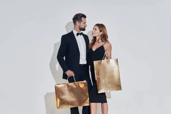 美丽的一对恋人背着金色的购物袋，站在灰色的背景下笑着 — 图库照片