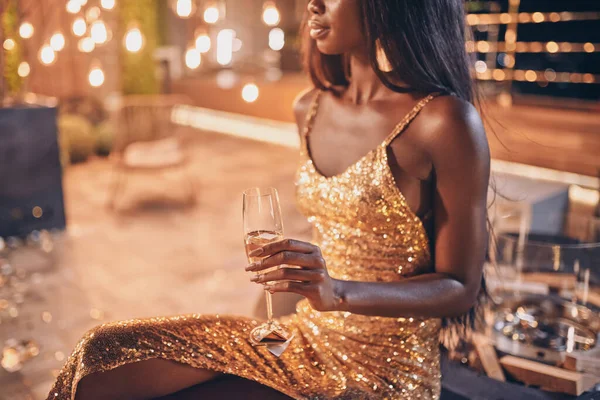 Mulher africana bonita em vestido de noite segurando flauta com champanhe enquanto passa o tempo na festa da noite — Fotografia de Stock