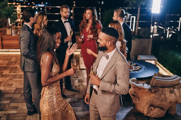 Grupo de jóvenes guapos en ropa formal comunicándose y sonriendo mientras pasan tiempo en una fiesta de lujo — Foto de Stock