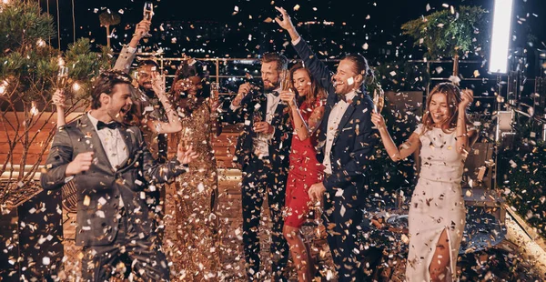 Eine Gruppe fröhlicher Menschen in Formalbekleidung tanzt und amüsiert sich mit herumfliegendem Konfetti — Stockfoto