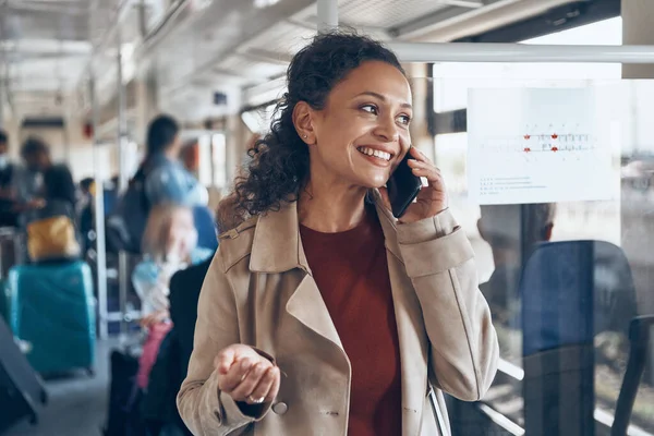 Mulher madura bonita usando telefone inteligente e sorrindo enquanto viaja de trem — Fotografia de Stock