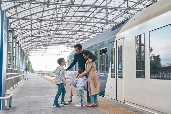 Plná délka šťastné rodiny se dvěma malými dětmi sbližování při stání na nástupišti železniční stanice spolu — Stock fotografie