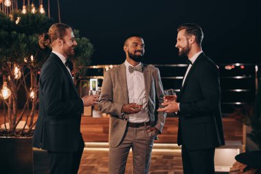 Takım elbiseli üç yakışıklı adam viski içip eğlenirken iletişim kuruyor.