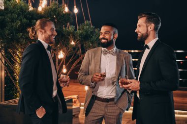 Takım elbiseli üç yakışıklı adam viski içip eğlenirken iletişim kuruyor.