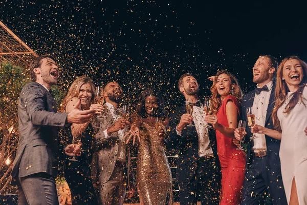 Groep gelukkige mensen in formele kleding hebben plezier samen met confetti vliegen rond — Stockfoto