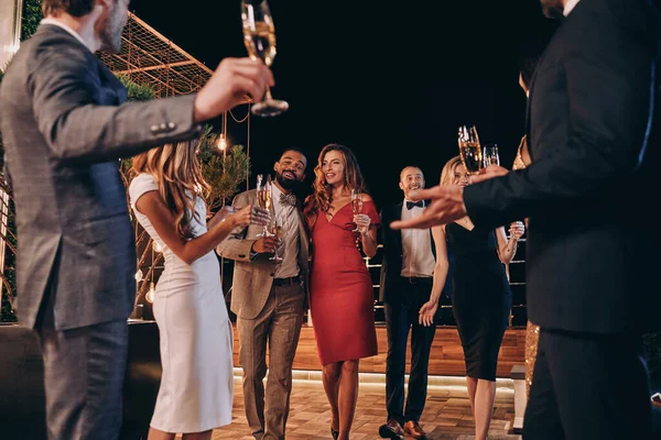 Grupo de jóvenes guapos en ropa formal comunicándose y sonriendo mientras pasan tiempo en una fiesta de lujo —  Fotos de Stock