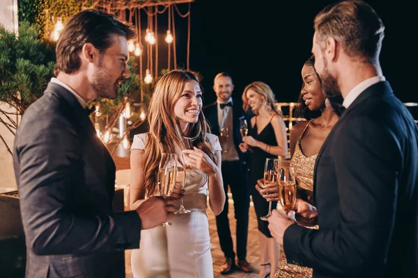 Grupo de personas en ropa formal comunicándose y sonriendo mientras pasan tiempo en una fiesta de lujo — Foto de Stock