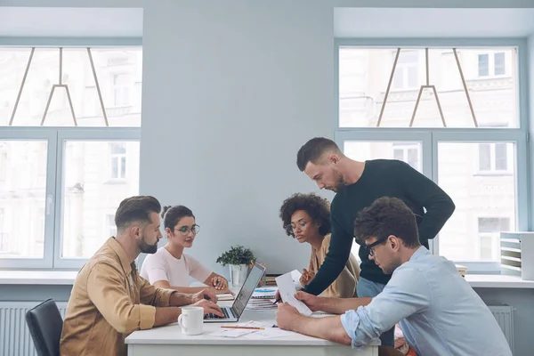 Grupo de jovens confiantes em roupas casuais inteligentes discutindo negócios enquanto se reúnem no escritório — Fotografia de Stock