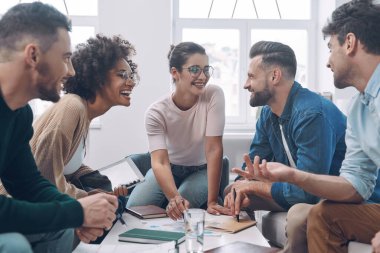 Bir grup modern genç iş tartışıyor ve ofiste birlikte otururken gülümsüyor.