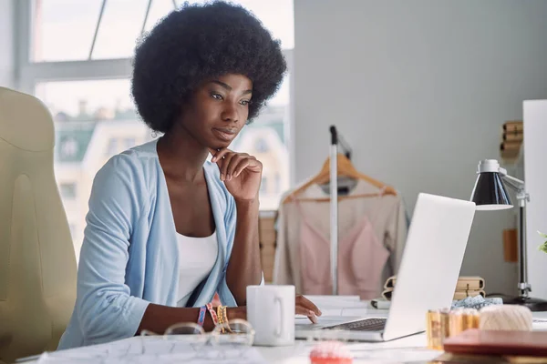 Gyönyörű fiatal afrikai nő használja laptop, miközben dolgozik a design stúdió — Stock Fotó