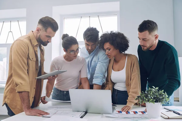 Gruppe selbstbewusster junger Leute in schicker Freizeitkleidung diskutiert Geschäfte, während sie am Schreibtisch im Büro steht — Stockfoto