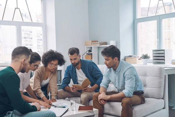 Sekelompok anak muda modern mendiskusikan bisnis sambil duduk di kantor bersama-sama — Stok Foto