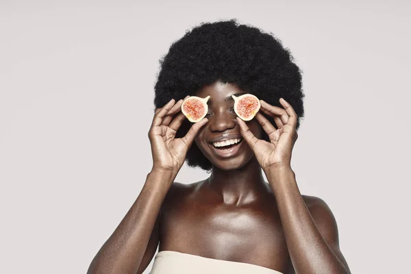 Egy gyönyörű, fiatal afrikai nő portréja, aki fügeszeletekkel és mosollyal takarta el a szemét. — Stock Fotó
