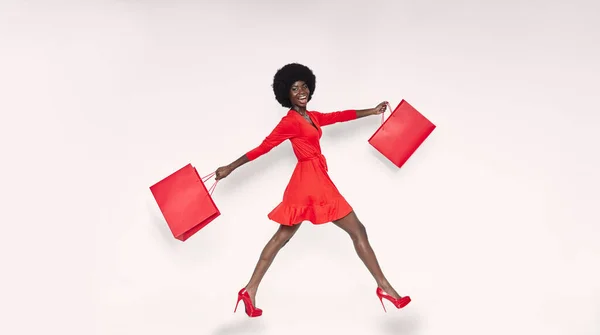 Pełna długość pięknej młodej Afrykanki w czerwonej sukience niosącej czerwone torby na zakupy — Zdjęcie stockowe