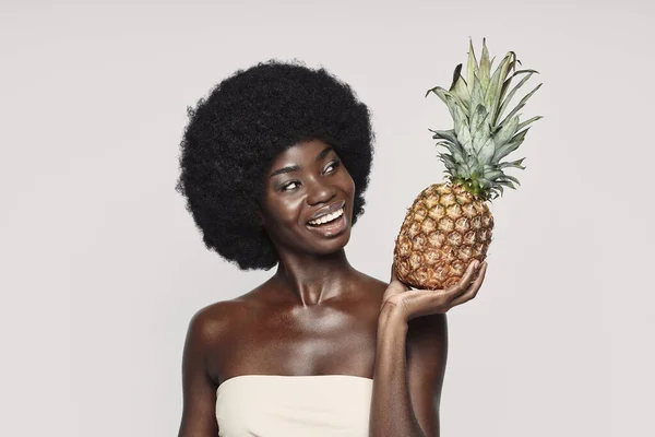 회색 배경에 맞서서 파인애플을 들고 미소짓고 있는 아름다운 아프리카 여자의 모습 — 스톡 사진