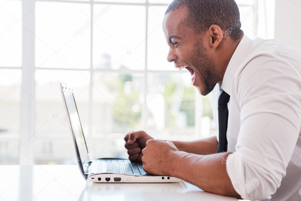 African man in shirt and tie shouting looking at laptop