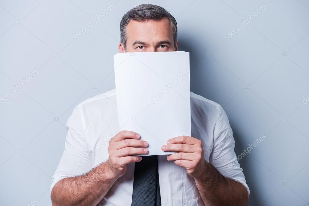 Mature man in formalwear hiding face behind documents