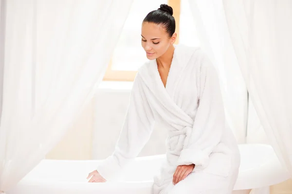 Woman in bathrobe touching water in bathtub — Stock Photo, Image