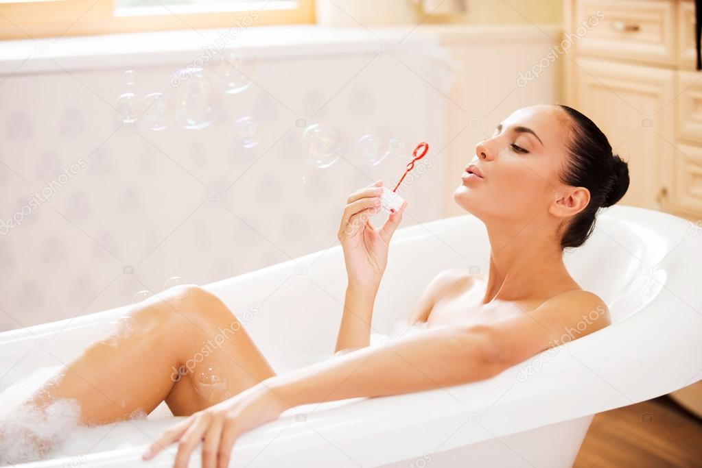 Woman blowing soap bubbles in bath