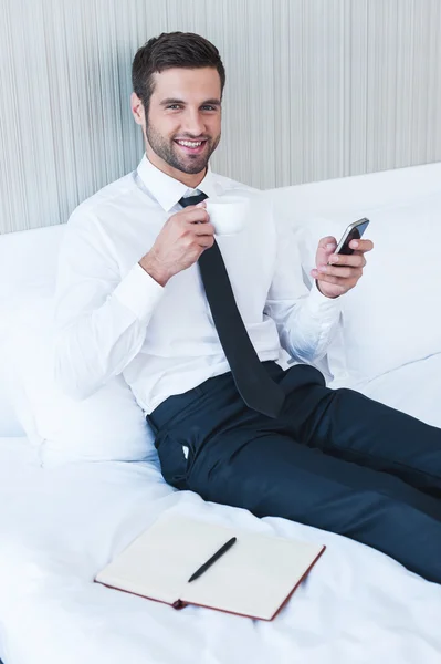 Чоловік у сорочці і краватці п'є каву і тримає мобільний телефон — стокове фото