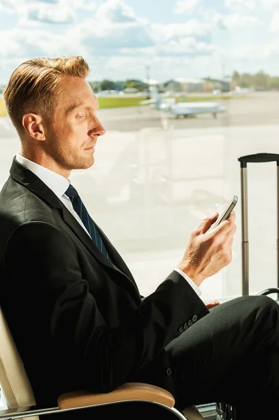 Businessman holding mobile phone in airport — Stock Photo, Image