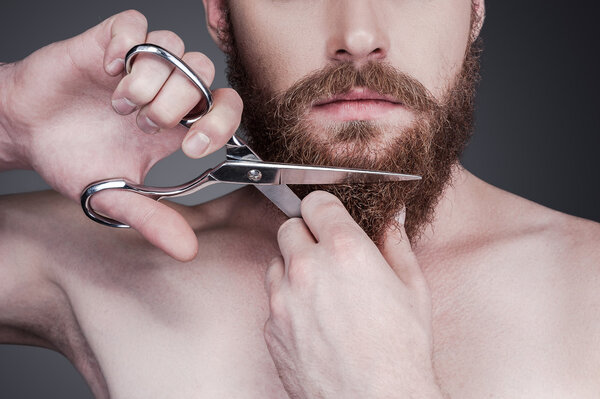 Shirtless man cutting his beard with scissors