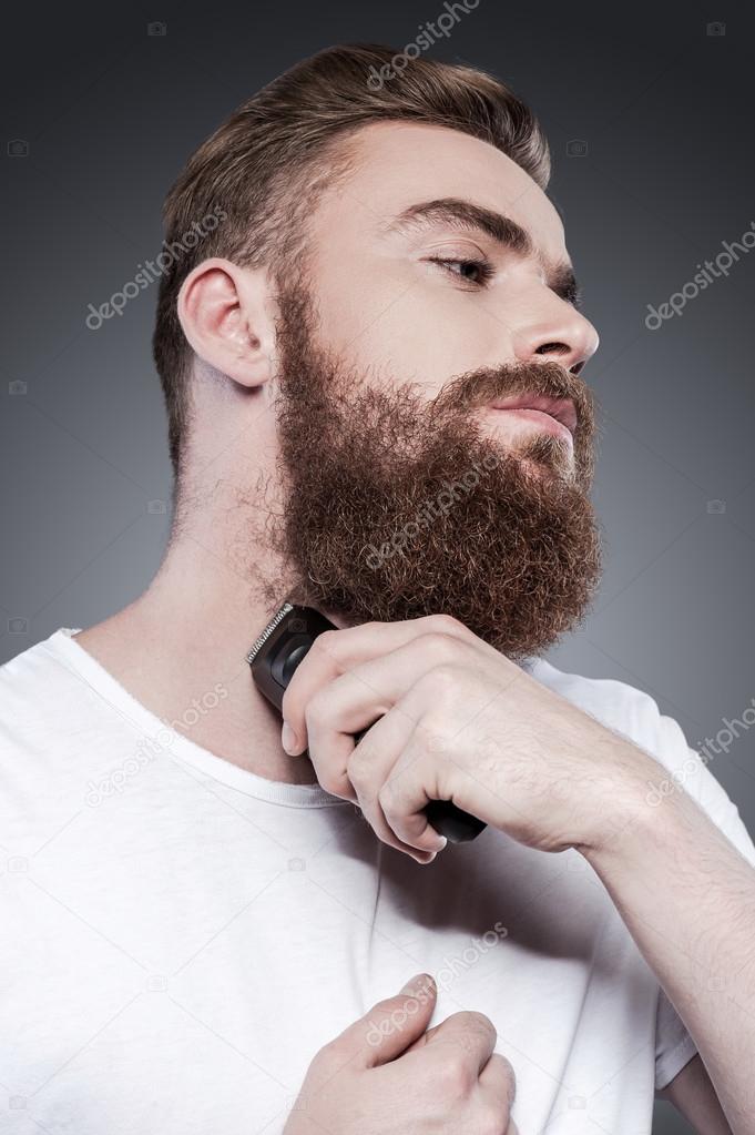 Young bearded man shaving with electric razor