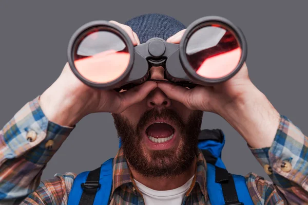 Uomo barbuto che trasporta zaino e guardando attraverso il binocolo — Foto Stock