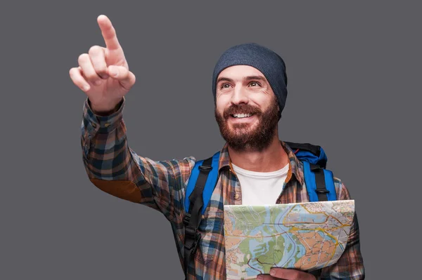 Barbudo hombre con mochila sosteniendo mapa y apuntando lejos — Foto de Stock