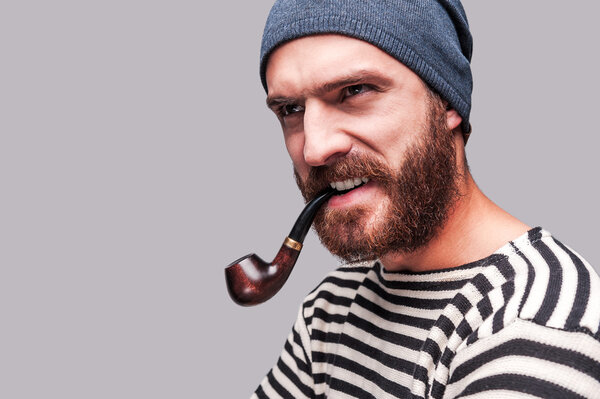 Бородатый мужчина в полосатой одежде курит трубку
