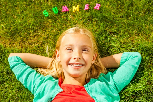 Gadis kecil memegang berbaring di rumput dengan plastik berwarna-warni huruf — Stok Foto