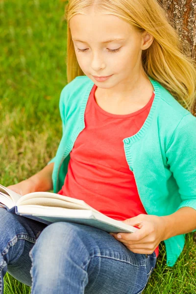 Kleines Mädchen liest Buch während es auf grünem Gras sitzt — Stockfoto