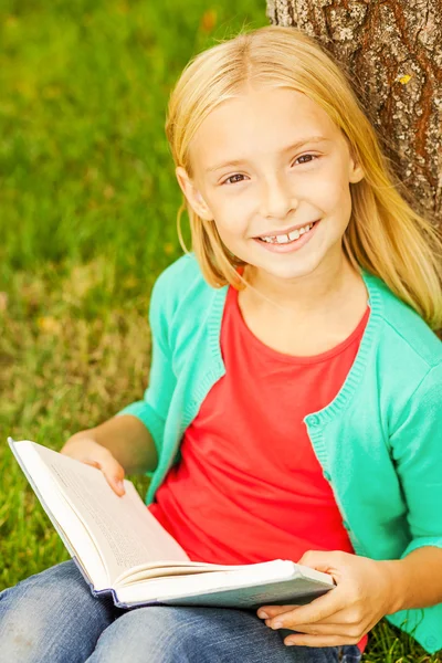 Blonde fille de cheveux tenant livre assis sur l'herbe verte — Photo