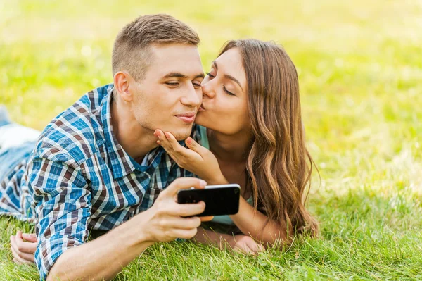 Pareja acostada en la hierba y tomando fotos de sí mismos —  Fotos de Stock