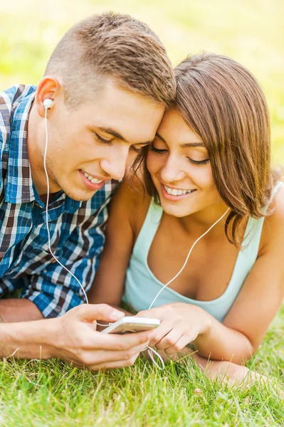 Pareja acostada en la hierba y eligiendo música en el teléfono —  Fotos de Stock