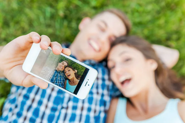 Amante casal fazendo selfie deitado na grama . — Fotografia de Stock