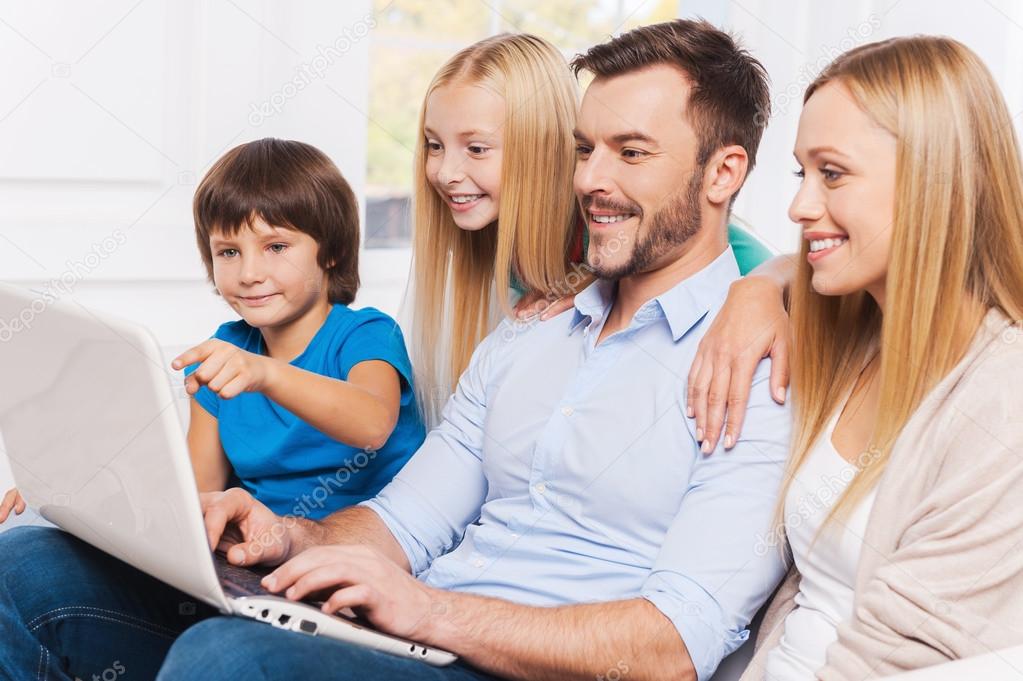 Happy family of four surfing net at laptop
