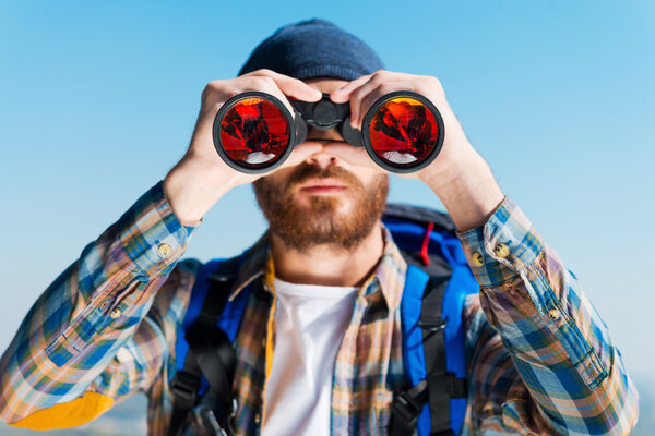 Человек с рюкзаком и смотрит в бинокль
