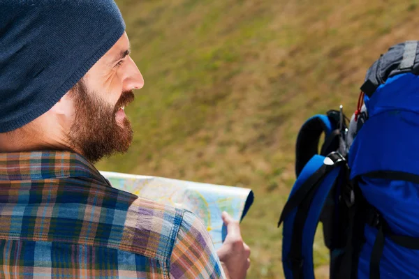 Hombre sentado cerca de la mochila sosteniendo mapa — Foto de Stock