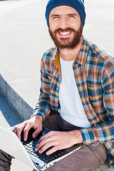 Skäggig man leende medan du arbetar på laptop — Stockfoto