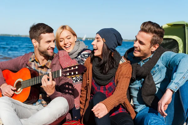 Young cheerful people sitting at the riverbank — Stock Photo, Image