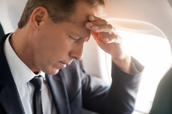 Businessman touching his forehead in airplane — Stock Photo, Image