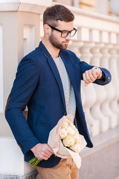 Hombre sosteniendo flores y mirando el reloj — Foto de Stock