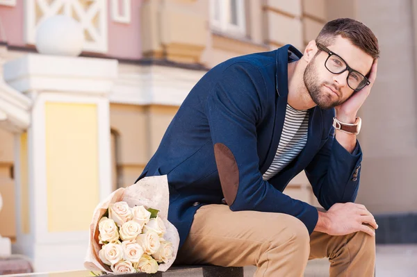 Frustrerad ung man sitter på bänken med blommor — Stockfoto